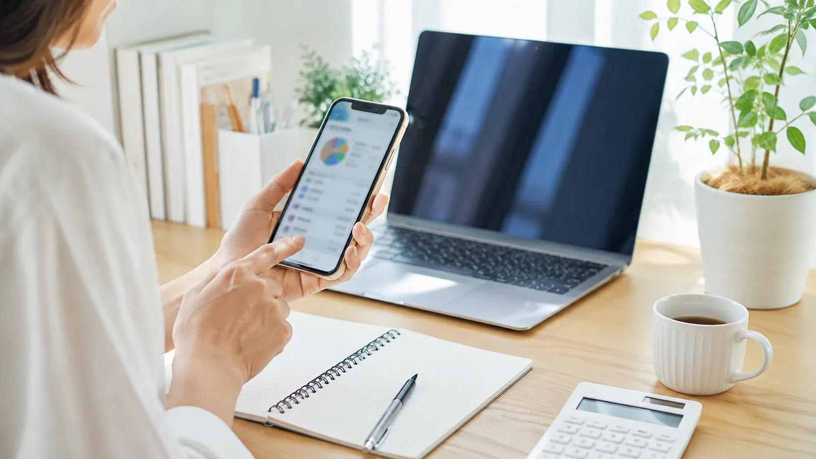 整ったデスクでスマホの家計管理アプリを確認している、お金の管理がきちんとした人の手元