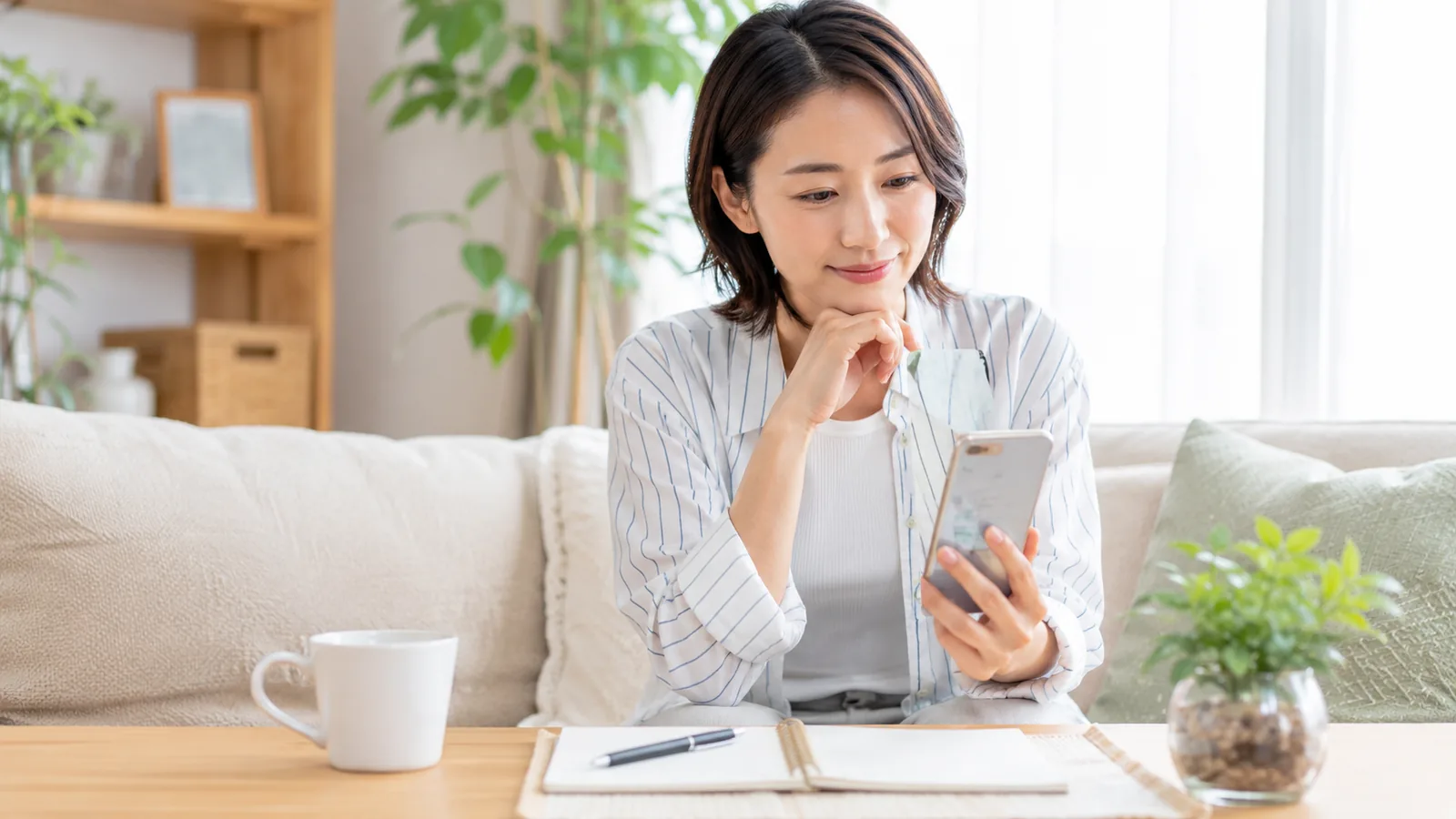 明るいリビングでスマホのサブスク一覧を確認しながら、家計を見直している様子