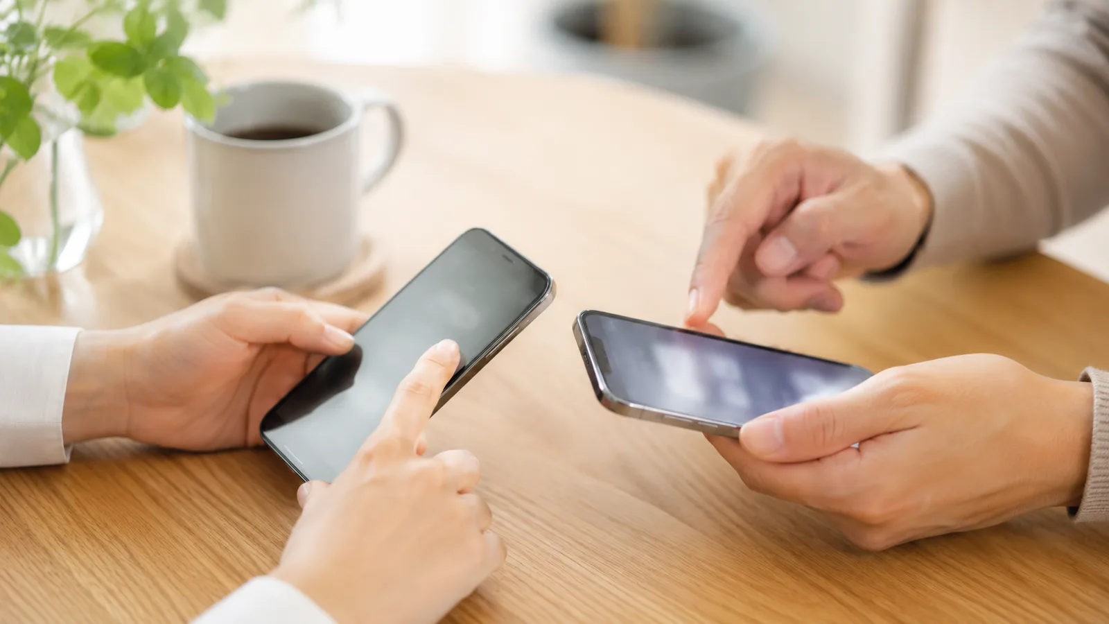 夫婦が2台のスマホを並べて、パスワード共有の設定を一緒に進めている手元