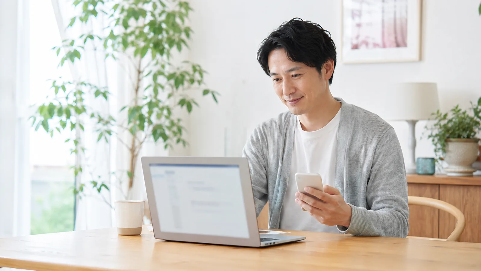 ダイニングテーブルでノートパソコンとスマホを使い、受信トレイのメールを整理する人