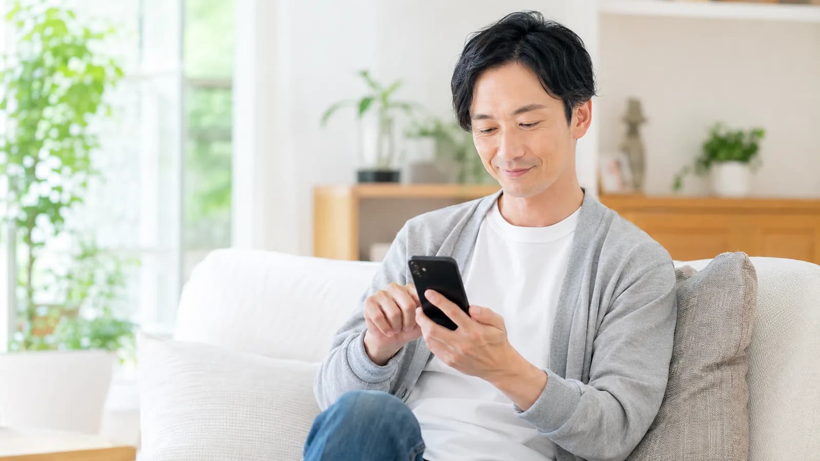 リビングのソファでスマホの写真アプリを開き、たまった写真を整理している人
